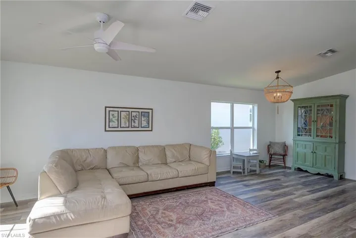 Living room featuring ceiling fan with notable chandelier, wood finished floors, visible vents, and baseboards