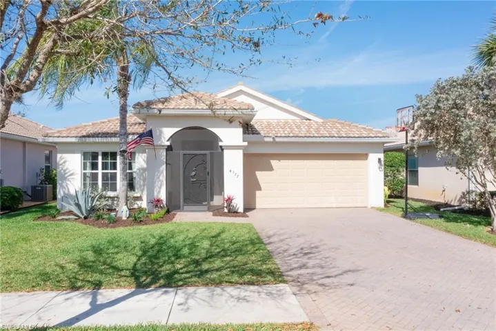 Ranch-style home featuring an attached garage, a tiled roof, decorative driveway, stucco siding, and a front yard