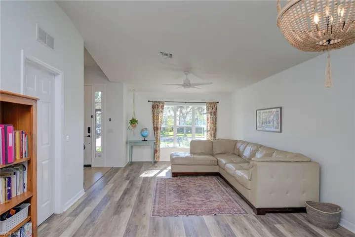 Living room with ceiling fan with notable chandelier, wood finished floors, visible vents, and baseboards