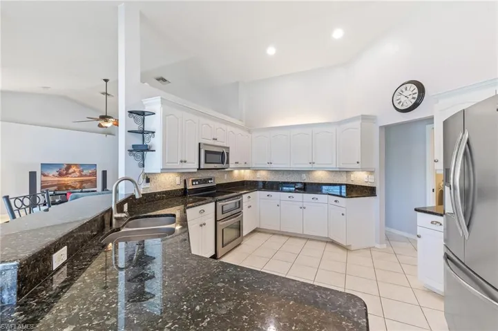Kitchen featuring stainless steel appliances, white cabinetry, lofted ceiling, and decorative backsplash