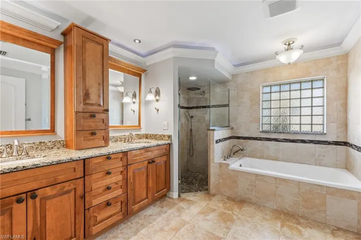 Bathroom featuring double vanity, a walk in shower, a garden tub, and crown molding