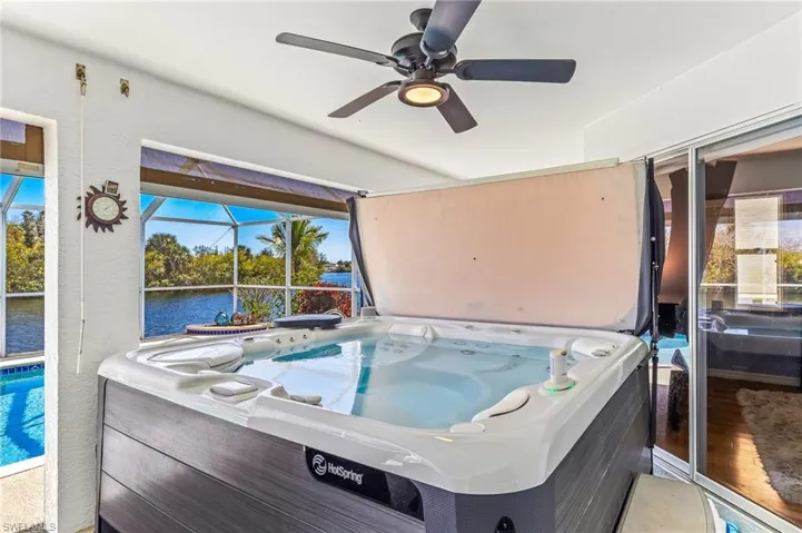 View of patio / terrace with a hot tub, a sunroom, screen enclosure, ceiling fan, and a water view