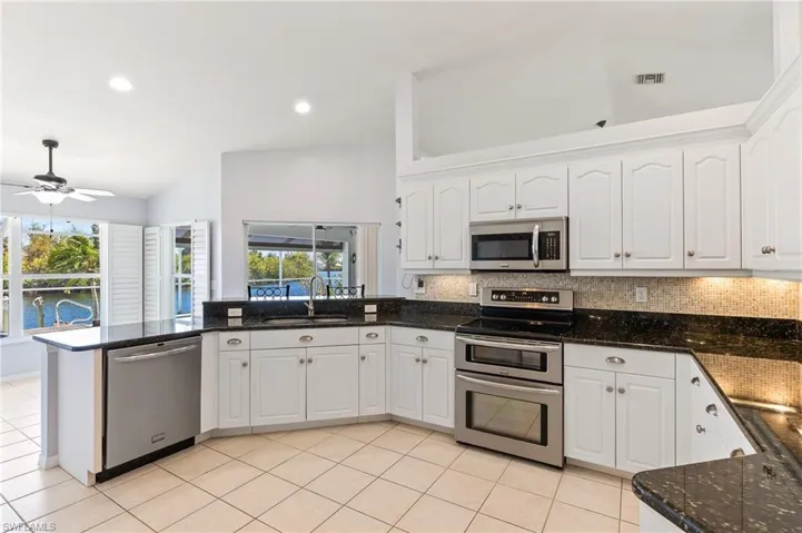Kitchen featuring white cabinets, tasteful backsplash, stainless steel appliances, lofted ceiling, and dark stone counters