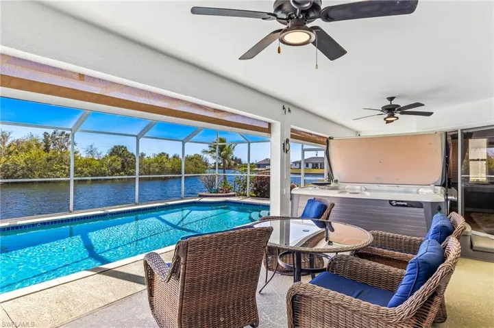 Outdoor pool with screen enclosure, a hot tub, a water view, and a patio