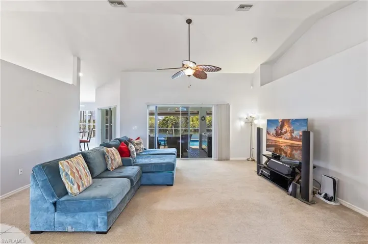 Living room with lofted ceiling, a ceiling fan, and light colored carpet