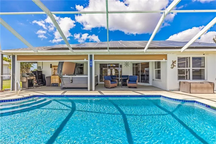 Swimming pool featuring a hot tub, screen enclosure, a grill, and a patio area