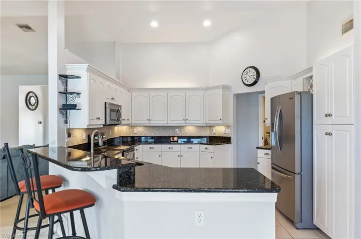 Kitchen with a peninsula, backsplash, stainless steel appliances, a high ceiling, and a kitchen breakfast bar