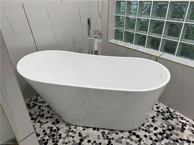 Freestanding soaking tub with a floor-mounted faucet, complemented by glass block window, and mosaic pebble tile flooring