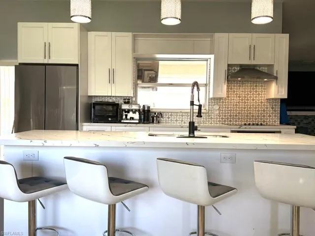 Kitchen featuring white shaker cabinetry, stainless steel refrigerator, patterned tile backsplash, peninsula with white countertops, and three pendant light fixtures