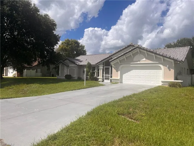 Concrete driveway leading to a two-car garage, tiled roof, stucco exterior, and mature tree