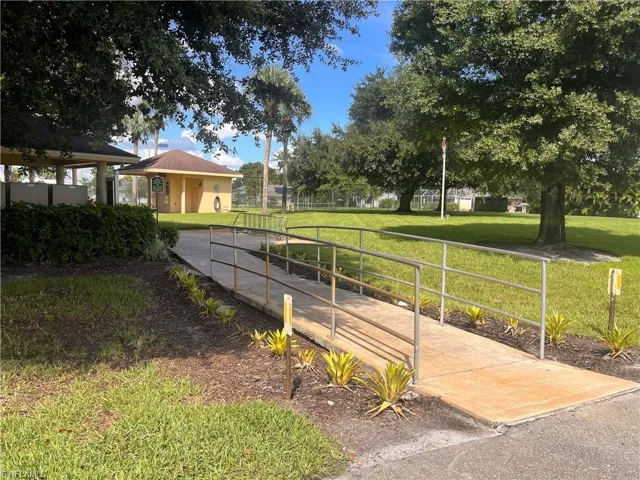 Concrete ramp with metal railings, surrounded by established landscaping and mature trees