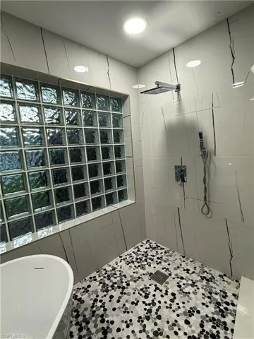 Glass block window, white tiled walls with dark veining, rainfall shower head, handheld shower fixture, and a mosaic pebble-style shower floor