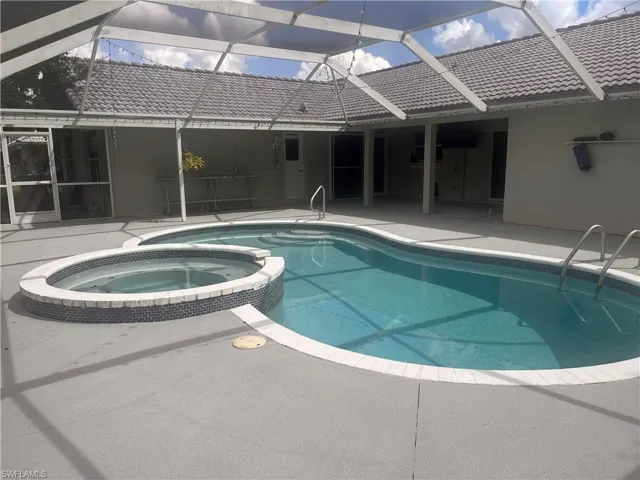 Screened pool enclosure featuring a custom-shaped pool, integrated spa with tile accents, and concrete decking
