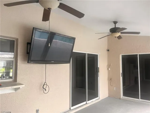 Covered patio featuring a textured wall finish, two ceiling fans, and multiple sliding glass doors