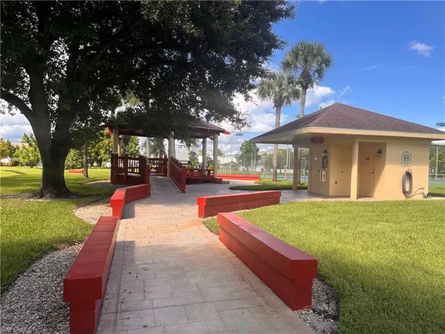 Paved pathway with red accent walls leading to a gazebo and a utility building