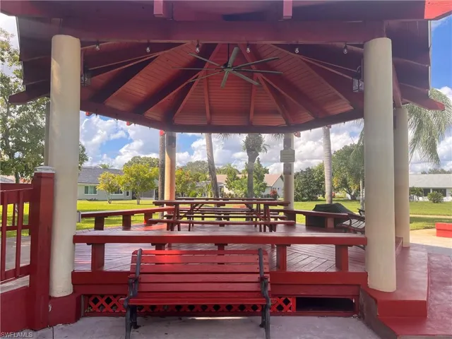 Red octagonal gazebo with a slatted roof, supported by light-colored pillars, featuring multiple built-in picnic tables and benches