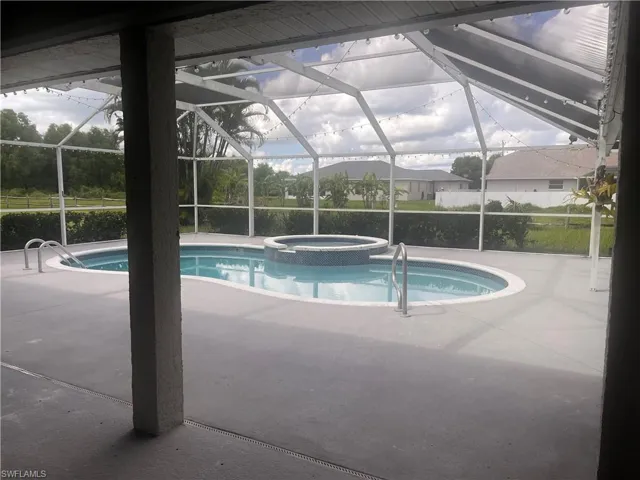 Screened-in outdoor living space featuring a freeform pool, integrated spa, and expansive concrete decking