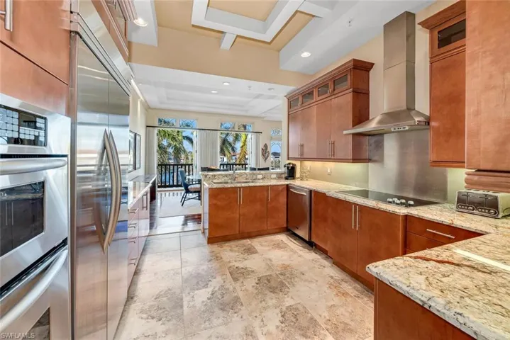 Kitchen with stainless steel appliances, light stone counters, a tray ceiling, kitchen peninsula, and wall chimney exhaust hood