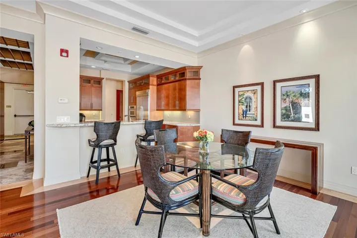 Kitchen with stainless steel appliances, light stone counters, a tray ceiling, kitchen peninsula, and wall chimney exhaust hood