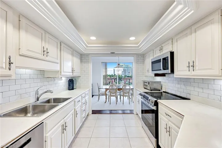 Kitchen with a tray ceiling, stainless steel appliances, light countertops, light tile patterned flooring, and recessed lighting