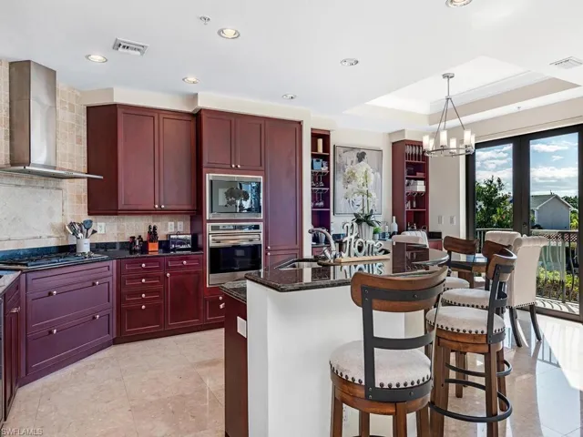 Kitchen featuring dark brown cabinets, wall chimney range hood, dark stone countertops, a breakfast bar, and recessed lighting