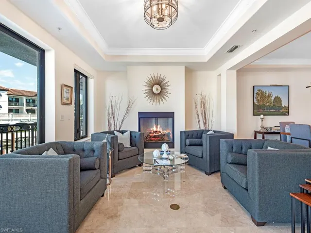 Living area with a warm lit fireplace, crown molding, a raised ceiling, and a chandelier