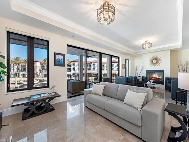 Living room featuring a raised ceiling, healthy amount of natural light, ornamental molding, and a chandelier