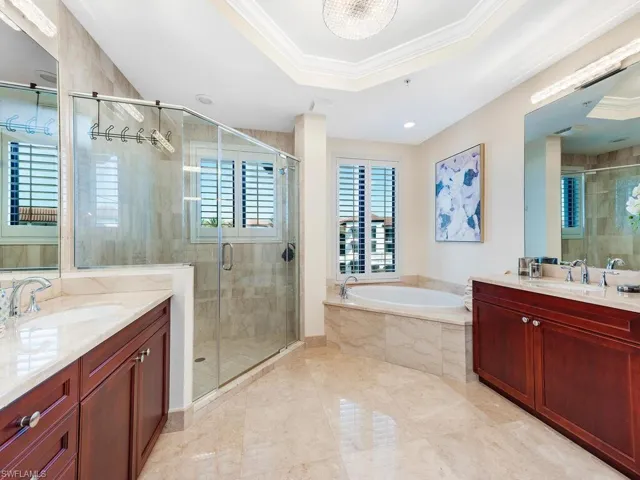 Full bath featuring crown molding, two vanities, a bath, a raised ceiling, and a stall shower
