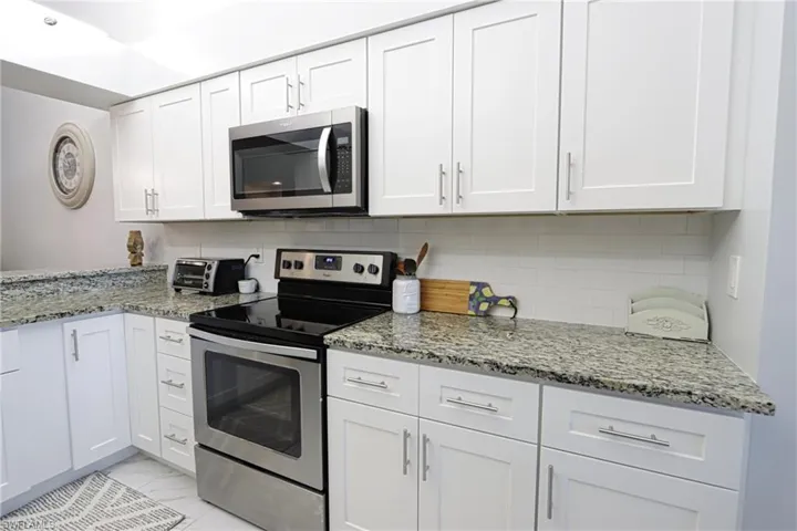 Kitchen with backsplash, light stone countertops, stainless steel appliances, and white cabinets