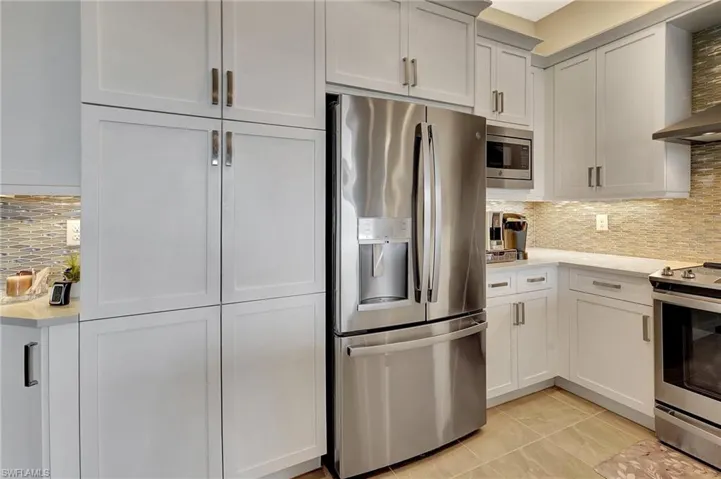 Kitchen featuring light tile patterned flooring, light countertops, tasteful backsplash, appliances with stainless steel finishes, and wall chimney range hood