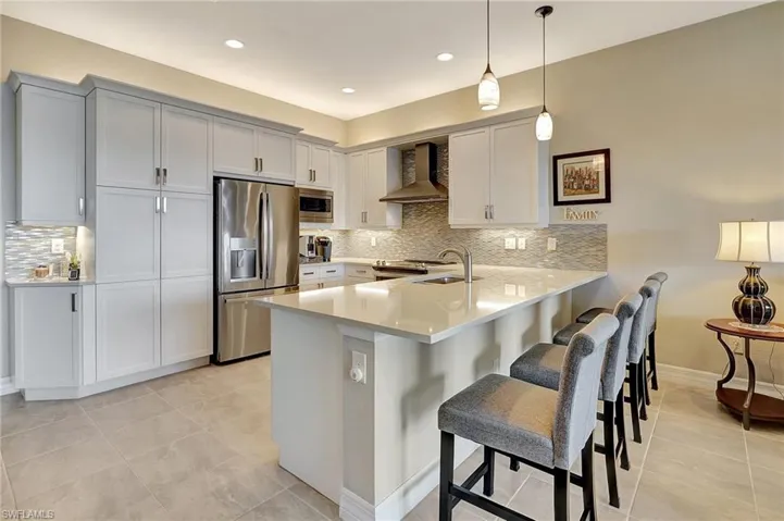 Kitchen featuring a sink, a breakfast bar area, appliances with stainless steel finishes, a peninsula, and wall chimney range hood