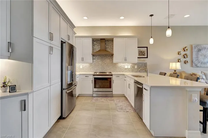 Kitchen with a sink, tasteful backsplash, a peninsula, stainless steel appliances, and wall chimney range hood