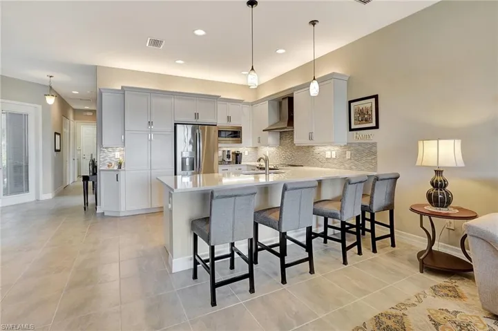 Kitchen featuring light countertops, a peninsula, wall chimney exhaust hood, stainless steel appliances, and a breakfast bar area