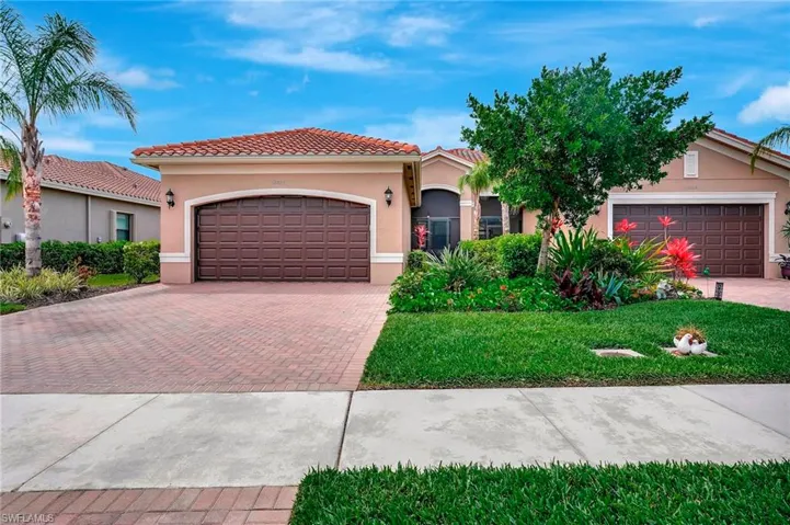 Mediterranean / spanish house featuring stucco siding, an attached garage, a tiled roof, decorative driveway, and a front yard