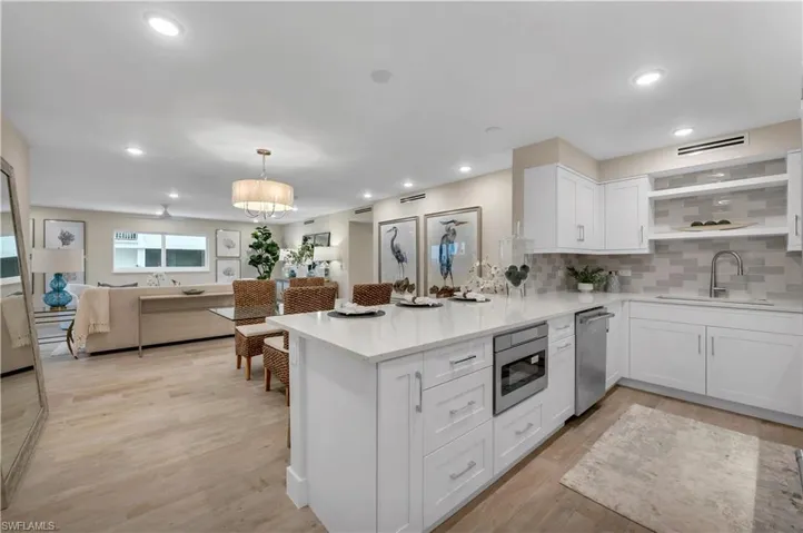 Kitchen featuring light hardwood / wood-style floors, kitchen peninsula, tasteful backsplash, white cabinets, and appliances with stainless steel finishes