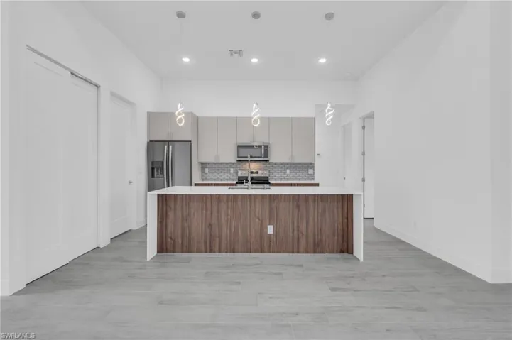 Kitchen featuring decorative backsplash, light countertops, appliances with stainless steel finishes, an island with sink, and light wood finished floors