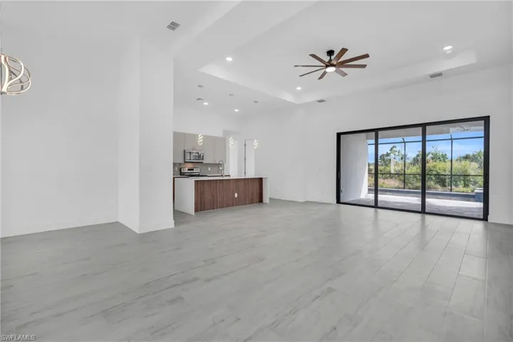 Unfurnished living room with a raised ceiling, light wood-style floors, ceiling fan, recessed lighting, and a high ceiling