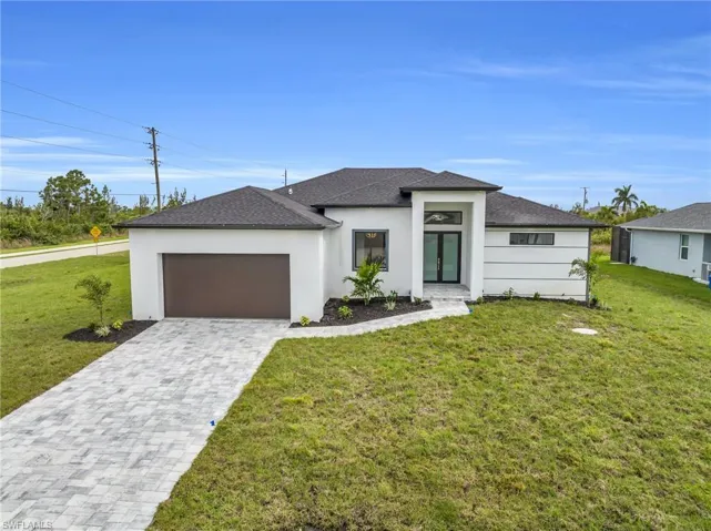 Prairie-style home with a front lawn, stucco siding, decorative driveway, a garage, and roof with shingles