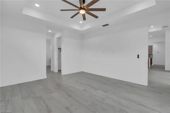 Unfurnished room featuring a raised ceiling, recessed lighting, light wood-type flooring, and a ceiling fan