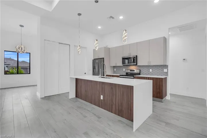 Kitchen with backsplash, light countertops, stainless steel appliances, an island with sink, and recessed lighting
