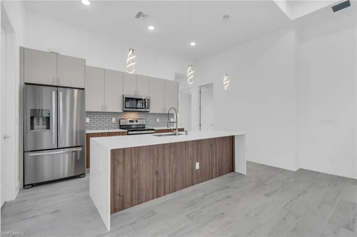 Kitchen with appliances with stainless steel finishes, gray cabinets, tasteful backsplash, light wood-style flooring, and light countertops