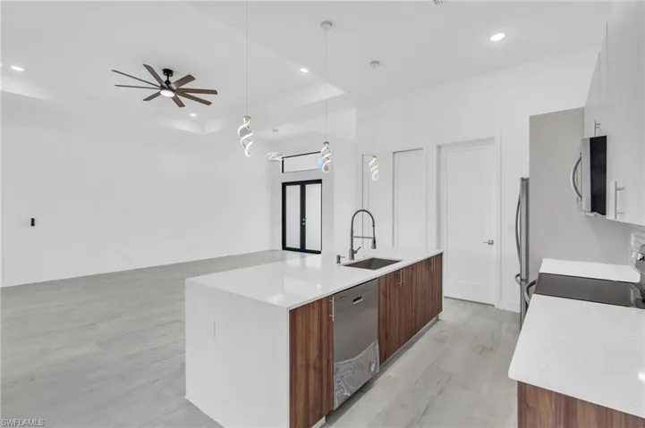 Kitchen with modern cabinets, light wood finished floors, recessed lighting, a kitchen island with sink, and a raised ceiling