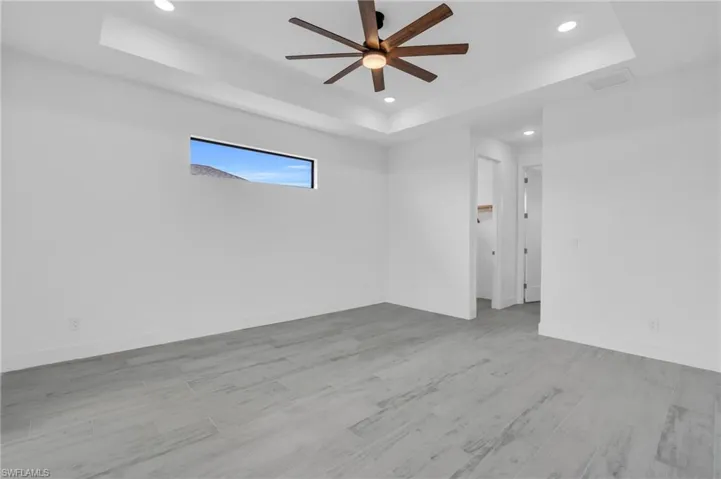 Unfurnished room with a raised ceiling, light wood-type flooring, recessed lighting, and a ceiling fan