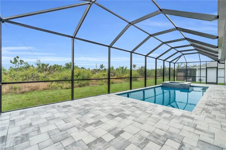 View of pool featuring a patio area, glass enclosure, a pool with connected hot tub, and a yard