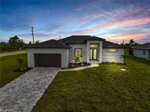 View of front of home with a yard, decorative driveway, an attached garage, and stucco siding