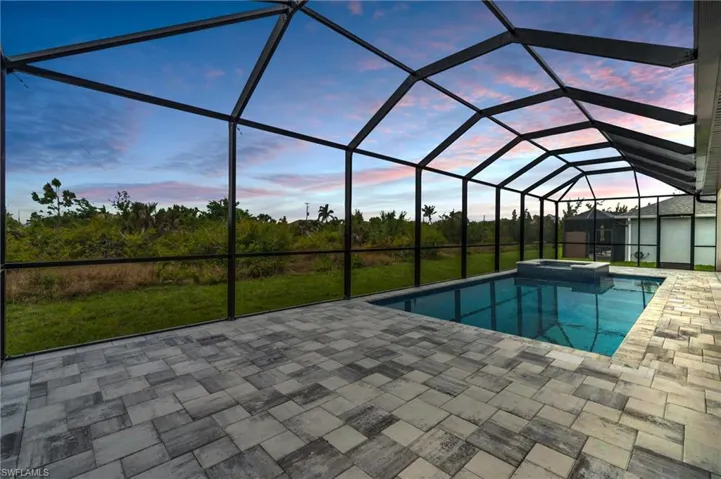 Pool at dusk featuring a lanai, a patio area, a pool with connected hot tub, and a lawn