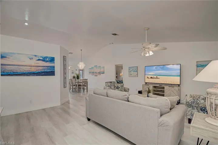 Living room with vaulted ceiling, light wood-style flooring, a chandelier, and a ceiling fan