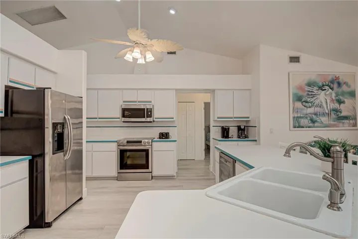 Kitchen featuring stainless steel appliances, white cabinets, light countertops, vaulted ceiling, and backsplash