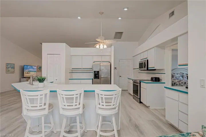 Kitchen featuring white cabinets, vaulted ceiling, a breakfast bar area, backsplash, and stainless steel appliances