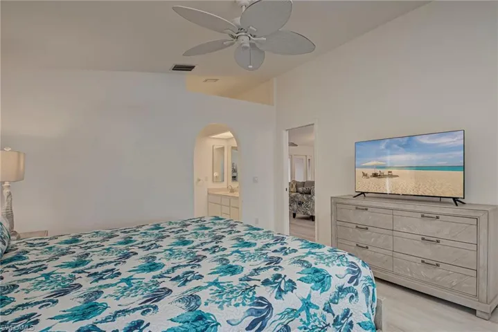 Bedroom featuring vaulted ceiling, a ceiling fan, arched walkways, light wood-type flooring, and connected bathroom